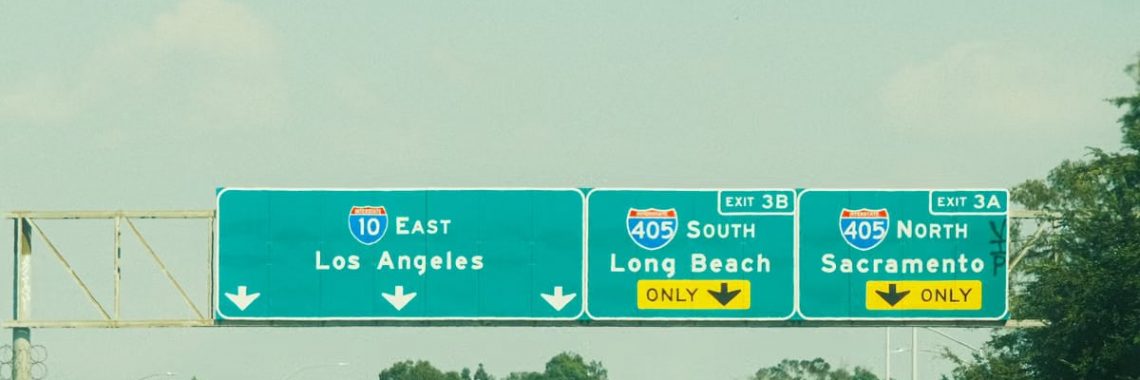 Highway signs with directions to Los Angeles, Long Beach, and Sacramento on a clear day.