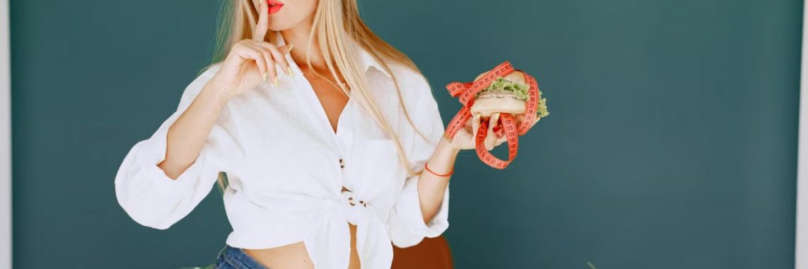 Woman holding a burger wrapped in measuring tape surrounded by fresh vegetables.