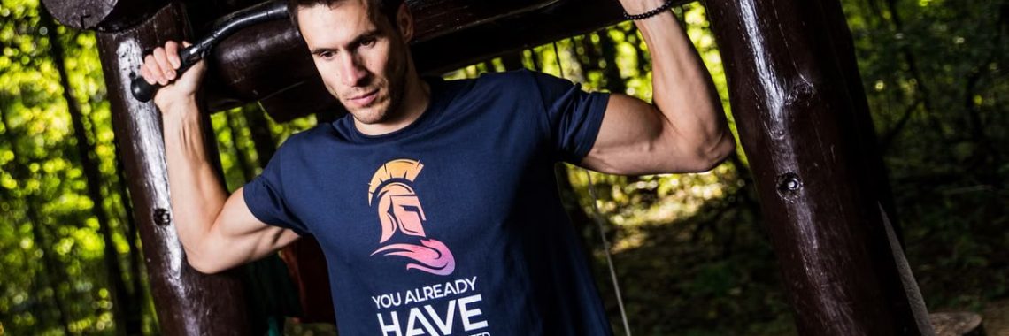 A man in a motivational t-shirt using an outdoor gym in a forest setting.